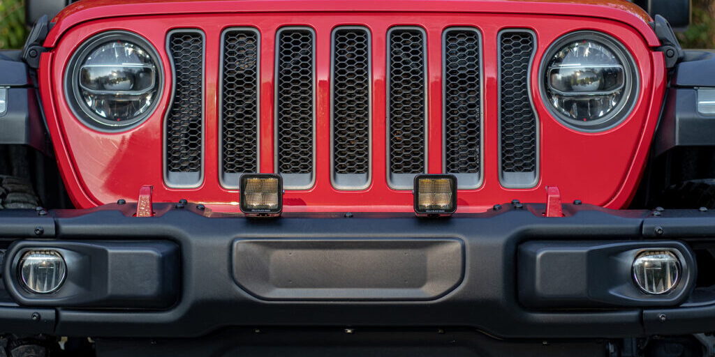 HELLA X-Treme Series LED Driving Lights in amber mode, X-shape position light, bumper-mounted on off-road SUV, IP69K auxiliary high-beam.