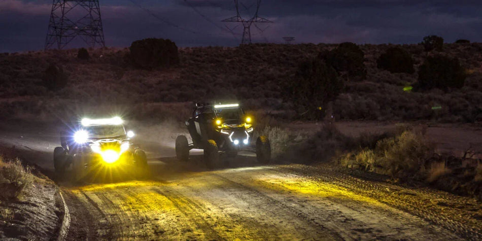 UTVs on rugged trail with HELLA X-Treme Series LED Driving Lights, IP69K, X-shape position light in white and amber modes, auxiliary high-beam for off-road use.